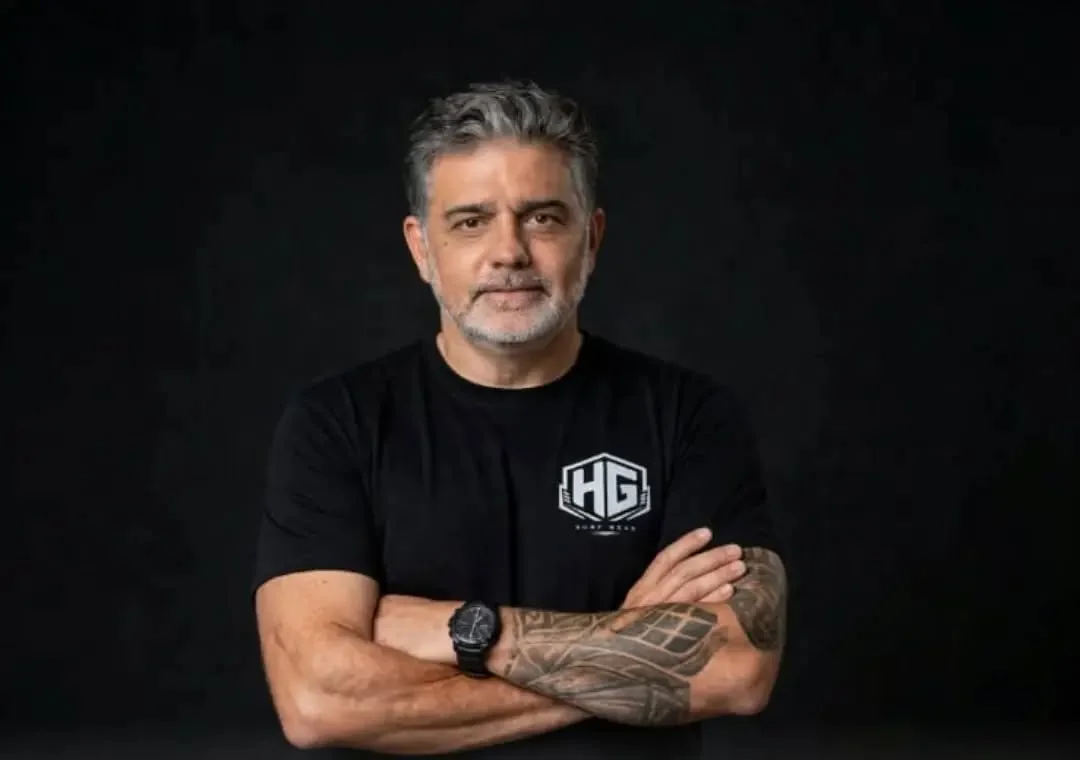 Henrique Guerra, criador da HG Surf Wear, de braços cruzados com a camiseta preta da marca